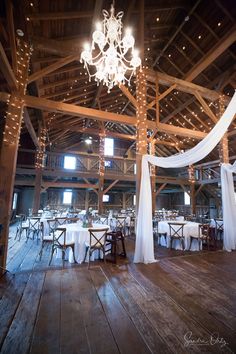 the inside of a barn decorated with white linens and chandelier hanging from the ceiling