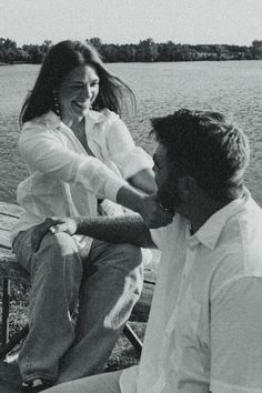 a man and woman sitting on a bench next to the water with their arms around each other