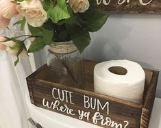 a wooden sign that says cut bums where you from? on the side of a toilet