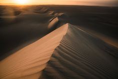 the sun is setting over an expanse of sand dunes in the middle of the desert