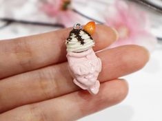 a hand holding a tiny pink and white doll with an ice cream cone on it's head