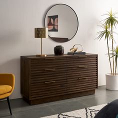 a large round mirror hangs on the wall next to a wooden dresser with gold accents