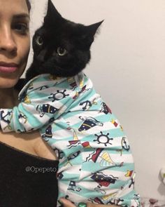 a woman holding a black cat wearing a shirt with airplanes all over it's sleeves