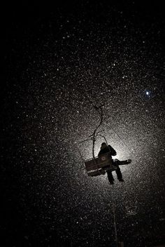 a person on a ski lift in the dark with snow falling all over them and stars above