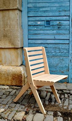 a wooden chair sitting in front of a blue door on a cobblestone street