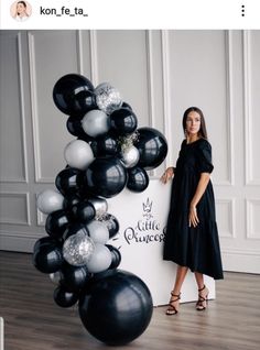 a woman standing next to a black and white balloon arch in front of a sign