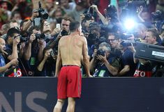 a shirtless man standing in front of a crowd of people with cameras around him