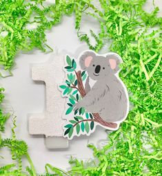 a koala sticker sitting on top of a green leafy tree next to the letter i