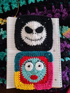 two crocheted notebooks with faces on them, one is black and the other is multicolored