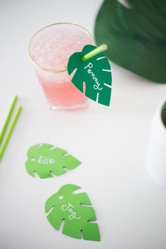 a drink and some paper cutouts on a white table with green straws next to it