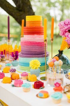 a table topped with lots of colorful cakes and cupcakes next to a tree