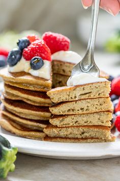 a stack of pancakes with fruit on top and a fork in the middle being held up