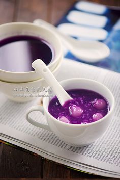 two white bowls filled with purple liquid on top of a table next to an open book