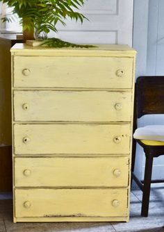 a yellow dresser sitting next to a chair and a potted plant on top of it