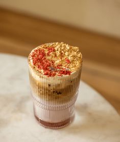 a cupcake sitting on top of a white table next to a glass filled with liquid