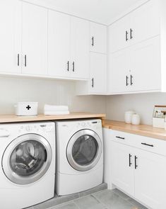 a washer and dryer in a white kitchen with wooden counter tops on the counters