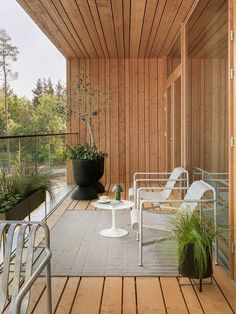 an outdoor deck with chairs and potted plants on the side, next to a wooden wall