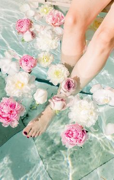 a woman's feet in the water with flowers floating around her and on top of them