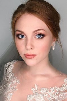 a woman with blue eyes wearing a wedding dress and veil on her head is looking at the camera