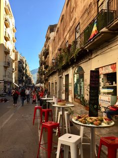 people are walking down the street in front of some buildings and tables with food on them