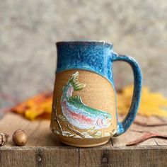 a coffee mug with a fish painted on it sitting on top of a wooden table