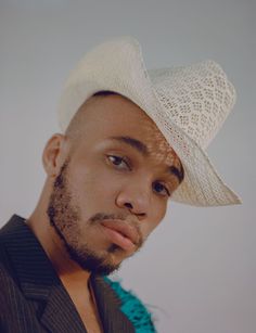 a man wearing a white cowboy hat looking at the camera with a serious look on his face