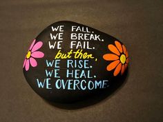 a painted rock that says we fall, we break, we fail, but then we rise, we heal, we overcome