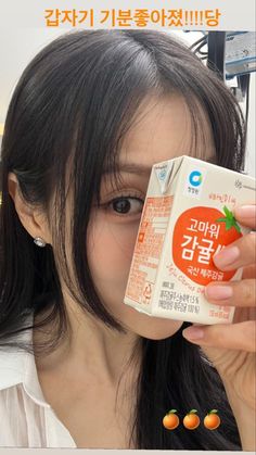 a woman holding up a carton of orange juice in front of her face and looking at the camera