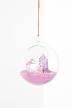 a glass ornament with rocks in it hanging from a rope against a white wall