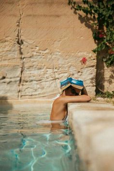 a woman is sitting in the water wearing a hat and reading a book on her head