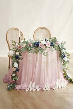 the table is covered with pink and blue flowers, greenery, and mr and mrs signs