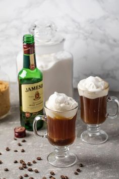 two glasses filled with hot chocolate and whipped cream next to bottles of booze, cookies, and coffee beans