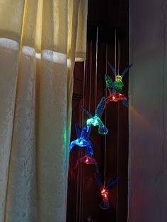 three colorful lights hanging from the side of a wall next to a window with curtains