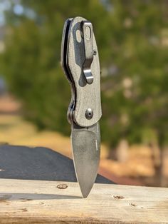 a knife is sitting on top of a piece of wood with trees in the background