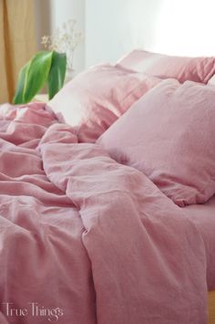 a bed with pink sheets and pillows on top of it, next to a plant