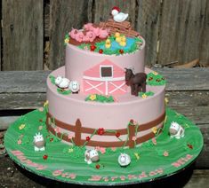 a pink and green cake with farm animals on the top is sitting in front of a wooden fence