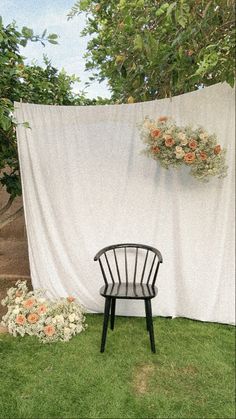 a black chair sitting in the grass next to a white curtain with flowers on it