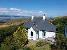 a white house sitting on top of a lush green hillside next to the ocean with mountains in the background