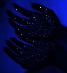 two black gloves with blue glitter on them are shown in the dark, against a blue background