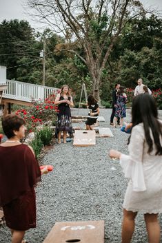 some people are playing games in the gravel near trees and flowers, while others look on