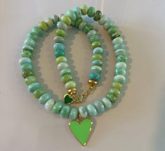 A unique and stylish necklace, perfect for summer days and nights. This 16-inch necklace features a beautiful blend of mint green and white opal rondelles, 8mm gemstone rondelles, and smooth pastel green beads. The piece is elegantly finished with a neon green colored heart-shaped gold-filled enamel charm. Secured with a lobster clasp closure, this versatile necklace can be dressed up or paired with jeans for a chic look. Its unique design and vibrant colors make it a must-have accessory for any outfit. Green Heart-shaped Beaded Necklace Gift, Green Heart-shaped Beaded Necklace, Green Jewelry With Heart Charm And Round Beads, 16 Inch Necklace, Stylish Necklace, Green Beads, Enamel Charms, Pastel Green, Green Bead