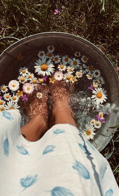 a person's feet in water surrounded by daisies