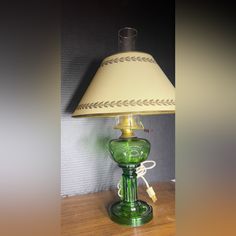 a green table lamp with a white shade on it's base sitting on a wooden table