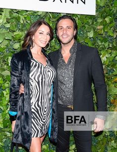 a man and woman standing next to each other in front of a wall with plants