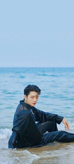 a young man sitting on the beach with his feet in the water