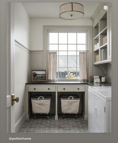 two laundry baskets sit in the middle of a small room with white cabinets and gray tile flooring