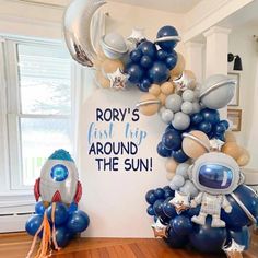 an astronaut balloon arch with balloons and heliums on the floor in front of it that says, rom's first trip around the sun