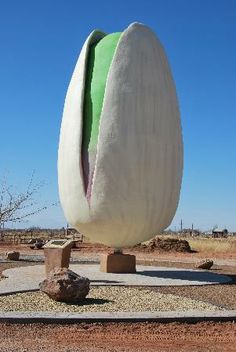 a large white and green sculpture in the middle of a dirt area with rocks around it