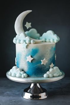 a blue and white cake with stars and moon decorations on the top is sitting on a silver plate