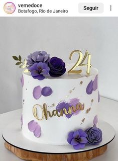 a white cake with purple flowers and gold numbers on the top is decorated with wooden slices